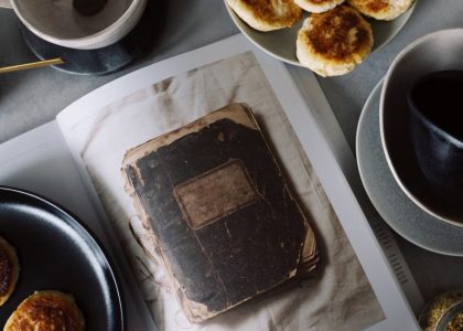A rustic breakfast arrangement with pastries, tea, and a vintage book in a cozy still life composition.