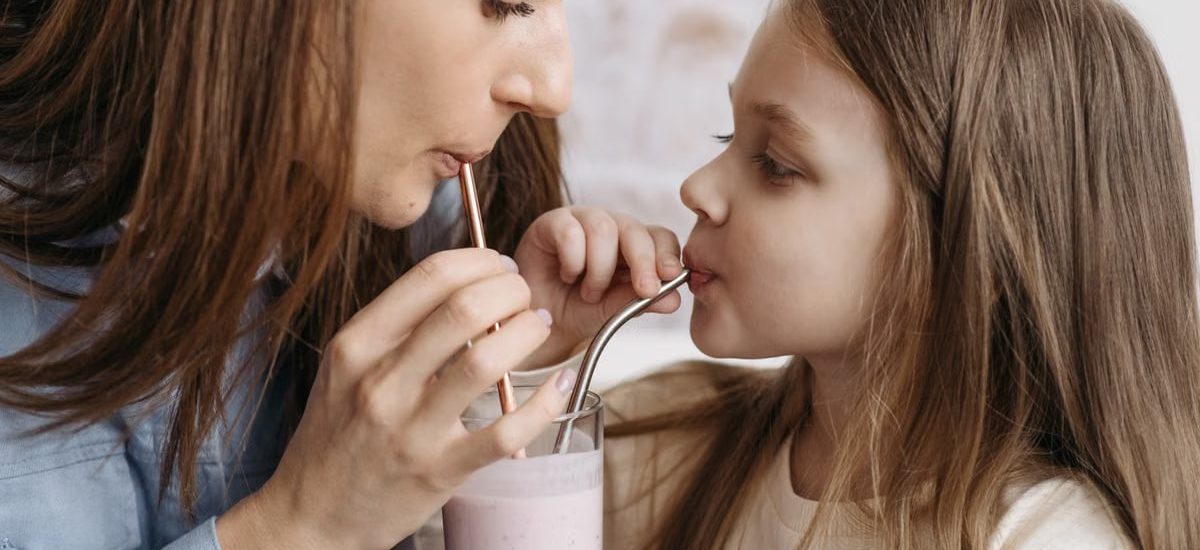 A mother and daughter sharing a strawberry milkshake indoors, depicting love and bonding.