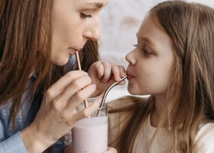 A mother and daughter sharing a strawberry milkshake indoors, depicting love and bonding.